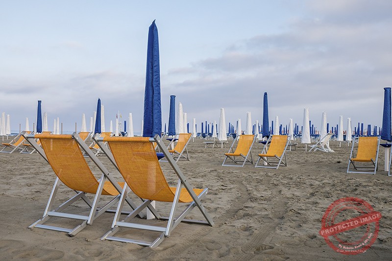 Pomarańczowe leżaki i niebieskie parasole na toskańskiej plaży