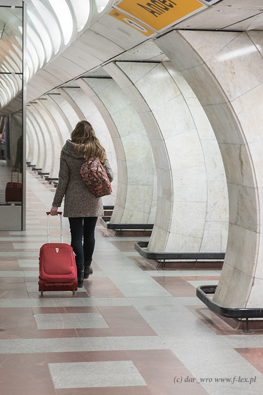 Kobieta z czerwoną walizką w praskim metrze